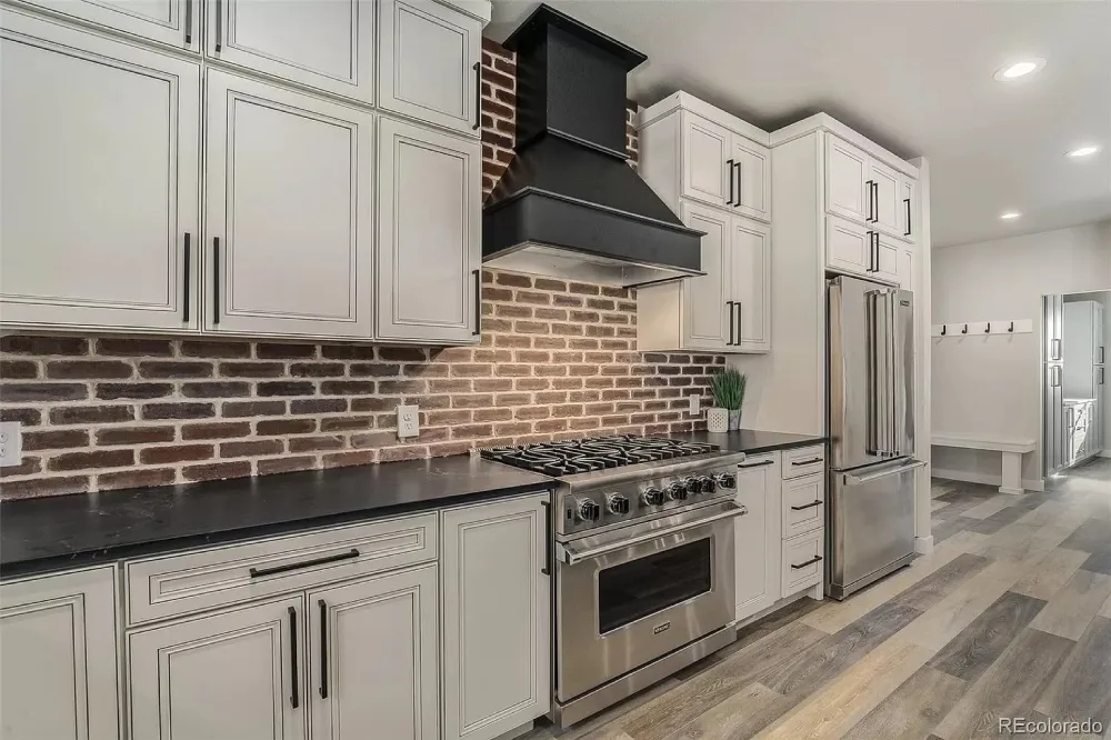 Custom white kitchen cabinets in Broomfield with brick backsplash and stainless steel range
